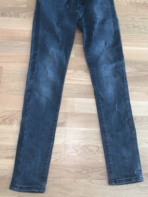 Svarta skinny jeans med slitningar - Säljer ett par svarta skinny jeans med slitningar och detaljer längs sidorna. Jeansen har klassisk femficksmodell och dragkedja. Perfekta för dig som gillar en edgy och trendig stil.
