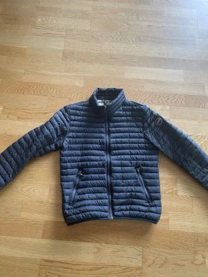 Mörkblå pufferjacka med dragkedja från colmar - Snygg mörkblå pufferjacka med hög krage och två framfickor med dragkedja. Jackan har quiltad design och en patch på ena ärmen. Perfekt för kalla dagar och ger en clean look till din outfit.