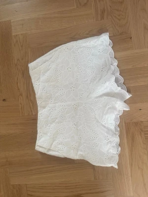Vita spetsdetaljerade shorts - Säljer ett par vita shorts med broderade blommor och fina spetsdetaljer längs kanterna.  Shortsen har en bekväm passform och är tillverkade i ett lätt bomullstyg.