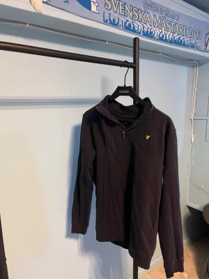 Mörkblå halvzip tröja med logga - Mörkblå långärmad tröja med halv dragkedja och liten gul logga på bröstet. Tröjan har hög krage och är tillverkad i ett mjukt material som passar perfekt till vardagslooken. Enkel och stilren design.