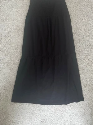 Svart långkjol från Kappahl - En svart långkjol från Kappahl i mjukt och bekvämt material. Kjolen har en enkel och stilren design med lätt utställd form och resår i midjan för skön passform. Perfekt till en sen sommarkväll. Skriv vid intresse💞passar xs, aldrig använd🥰