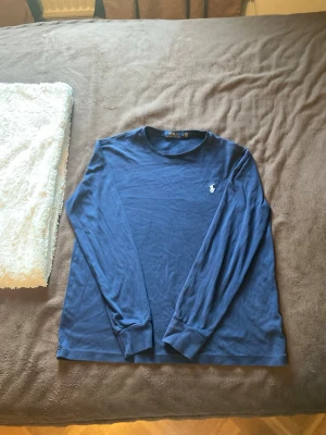 Blå långärmad tröja från Polo Ralph Lauren - Mörkblå långärmad tröja från Polo Ralph Lauren med klassisk rund hals och den ikoniska broderade loggan på bröstet. Tillverkad i mjuk bomull som känns skön mot huden. Perfekt till jeans eller chinos för en clean look.