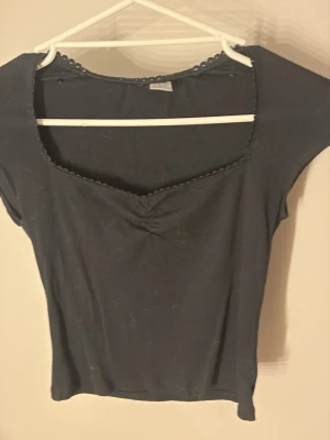 Svart topp med v-ringning - Snygg svart ribbad topp med v-ringad hals och dekorativ kant. Toppen har korta ärmar och lätt rynkning vid bysten för en extra detalj. Perfekt att styla med jeans eller kjol för en trendig look. Storlek S men passar även XS, använd 2 gånger. Har även en likadan tröja i röd som finns i min profil!!