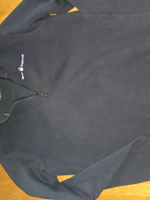 Marinblå Sail Racing fleece-tröja - Mörkblå fleece-tröja från Sail Racing med halv dragkedja och broderad logga på bröstet. Tröjan har hög krage och mjukt fleecefoder på insidan, perfekt för kyliga dagar. Sportig och stilren design.