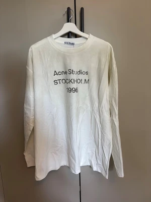 Vit långärmad t-shirt Acne Studios - Vit långärmad t-shirt från Acne Studios med tryck 'Acne Studios STOCKHOLM 1996' på bröstet. Klassisk rund hals och avslappnad passform. Tillverkad i mjuk bomull, perfekt för en clean och stilren look..                                Använd någon gång endast! Har ej kvitto! 