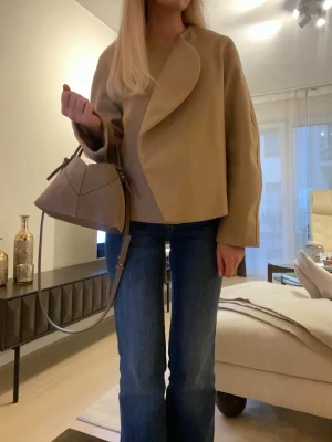 Beige kappa med oversized krage - Säljer denna superfina korta kappan med oversized asymmetrisk krage och rak passform. Kappan har långa ärmar och är tillverkad i ett mjukt, tjockare tyg som ger en lyxig känsla🤍 Storlek S