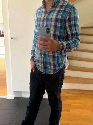 Rutig skjorta från Ralph Lauren - Säljer en klassisk rutig skjorta från Ralph Lauren i blå, grön och vit färgskala med inslag av lila och gul broderad logga på bröstet. Skjortan har lång ärm, knappar framtill och är tillverkad i mjuk bomull. Perfekt för en avslappnad men ändå stilsäker look. Sitter som small.