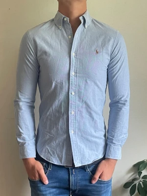 Ralph lauren skjorta - Säljer denna stiliga ljusblåa Ralph lauren skjorta! den är i mycket bra skick utan defekter! Den är i storlek S modell slim fit, den är 71 cm lång och 45 cm bred, hör av dig vid frågor!