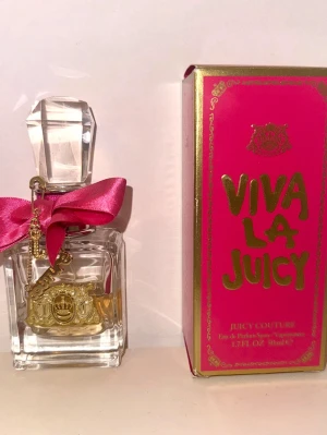 Viva La Juicy parfym från Juicy Couture 50ml - Viva La Juicy parfym från Juicy Couture i en elegant glasflaska med stor, slipad kork och en rosa sidenrosett. Flaskan har guldfärgade detaljer och en charm med logotyp. Förpackningen är starkt rosa med guldtext.