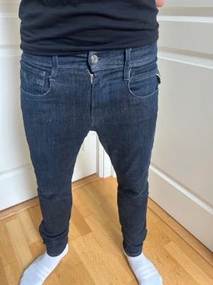 Svarta slim fit jeans herr - Säljer ett par svarta slim fit jeans med låg midja och smal passform. Jeansen har klassiska fem fickor, bälteshällor och dragkedja med knapp. Materialet är stretchigt denim som sitter tajt längs benen.