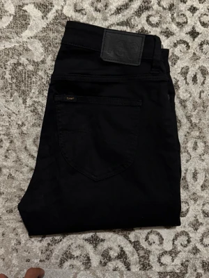 Svarta jeans från Lee - Snygga svarta jeans från Lee med klassisk femficksdesign och diskret logga på bakfickan. Jeansen har en rak passform och är tillverkade i ett mjukt denimtyg som sitter skönt hela dagen.