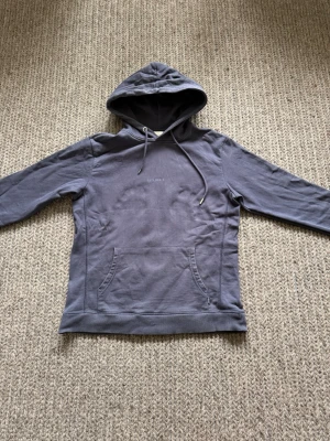 Mörkblå hoodie från Les Deux - Snygg mörkblå hoodie från Les Deux med minimalistisk logga på bröstet. Hoodien har huva med dragsko och en stor magficka. Tillverkad i mjukt bomullsmaterial och har långa ärmar. Perfekt för en avslappnad och stilren look.
