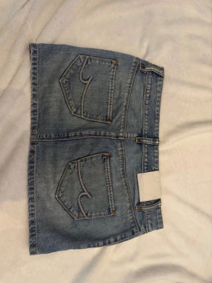 Blå jeanskjol med fickor - Snygg blå jeanskjol i kort modell med stora fickor både fram och bak. Kjolen har klassisk denimlook med synliga sömmar och knappstängning framtill. Märket är crocker och kjolen köptes på vinted men har endast används en gång sen dess