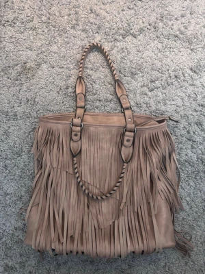 Beige väska - Snygg beige väska i mockaimitation med långa fransar och tvinnade handtag. 