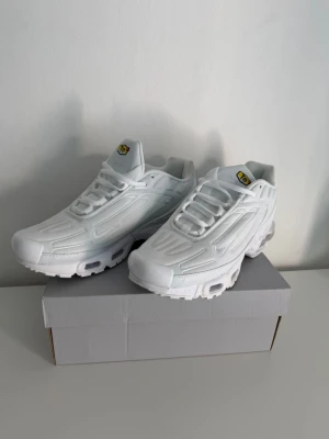 Vita Nike Air Max Plus TN sneakers - Säljer ett par helvita Nike Air Max Plus TN sneakers med klassisk mesh och syntetpaneler. Skorna har tydliga TN-loggor på plösen och hälen samt synlig Air-dämpning i sulan. Snygg och sportig siluett som passar till streetwear.
