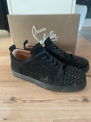 Christian loubutin med nitar - Snygga svarta sneakers i mocka från Christian Louboutin med svarta nitar på tån och svarta skosnören. Låg modell med klassisk siluett och diskret logga på hälen. Perfekta för dig som vill sticka ut med en edgy detalj. Alla nitar sitter på, 1 extra nit medföljer. Bra skick, inga skador endast lite smutsiga men de går att tvätta