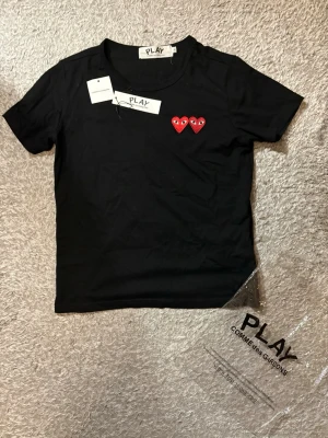 Commes des Garçons t shirt - Säljer nu denna svarta t shirt med röda hjärtan från Commes des garçons. Tröjan är använd endast 2 gånger och i perfekt skick. Storleken är S men den passar även som Xs och passar ca ~165/170. Tröjan kommer även med Cdg play påsen. OBS! Kragen vid tröjan är lite stor. Skriv vid fler frågor!