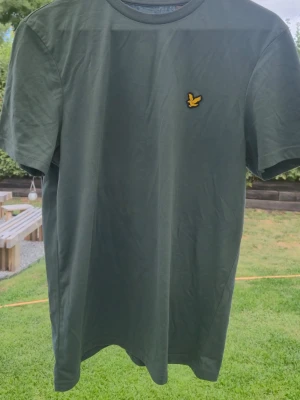 Blå t-shirt från Lyle & Scott - Snygg blå t-shirt från Lyle & Scott med klassisk gul logga på bröstet. T-shirten har rund halsringning och korta ärmar. Tillverkad i mjuk bomull som känns skön mot huden. Perfekt för en avslappnad och stilren look.