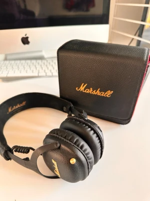 Marshall svarta over-ear hörlurar - Marshall over-ear hörlurar i svart konstläder med gulddetaljer och klassisk logga på kåporna. Medföljer matchande svart fodral med gul Marshall-text och röd kant. Snygg retrodesign och vadderad bygel för extra komfort.