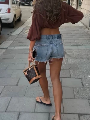 Brun och beige bucket bag med monogram - Snygg liten bucket bag i brunt och beige med monogrammönster och ljusa läderdetaljer. Väskan har dragskostängning med guldfärgade detaljer och kort handtag. Perfekt storlek för det viktigaste och ger en lyxig touch till din outfit.