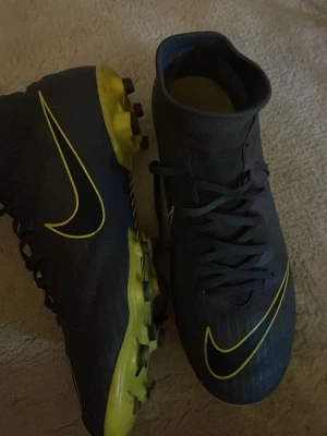 Svarta Nike fotbollsskor med gula detaljer - Säljer ett par svarta fotbollsskor . Grå svarta med gula detaljer 