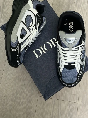 B30 sneakers i blå och vit - Säljer ett par B30 sneakers i blått, vitt och svart med grå detaljer. Skorna har en sportig design med mesh och läderpaneler, samt vita skosnören. Snygg logga på sidan och tungspetsen. Perfekta för dig som vill sticka ut med lyxig streetstyle.
