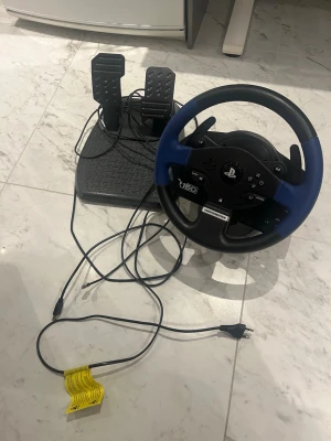 Thrustmaster T150 ratt och pedaler - Säljer en Thrustmaster T150 ratt och pedalset för PlayStation. Ratten har svart och blå färg med flera knappar och paddlar, och pedalerna är i svart plast med halkskydd. Perfekt för racing- och bilspel för en mer realistisk spelupplevelse.