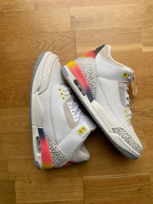 Vita sneakers med färgdetaljer - Säljer ett par vita sneakers med grå och beige detaljer samt färgade inslag i gult och rött på hälen. Skorna har en klassisk låg siluett, mönstrade partier vid tån och hälen samt vita skosnören. Materialet är en mix av läder och syntet.