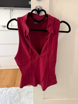 Mörkröd ärmlös topp med krage - Säljer en snygg mörkröd ärmlös topp med krage och djup v-ringning. Toppen har figurnära passform och är perfekt för dig som vill ha en stilren men ändå trendig look. 
