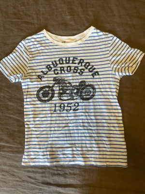 Stl.122/128 Randig t-shirt med motorcykeltryck H&M - Stl.122/128, en vit och blå randig t-shirt från H&M med coolt motorcykeltryck, bomull, 