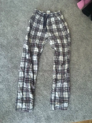 Rutiga pyjamasbyxor 158/164 - Säljer ett par rutiga pyjamasbyxor i vitt, marinblått och vinrött. Byxorna har resår i midjan med snörning för bästa passform. Perfekta för mysiga hemmakvällar eller lata morgnar. Tillverkade i mjukt och skönt material.