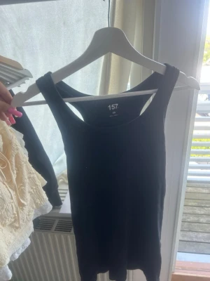 Svart ribbad linnetopp - Säljer en svart ribbad linnetopp med breda axelband. Perfekt att styla till jeans eller kjol för en enkel och clean look. Toppen är ärmlös och har en klassisk, tight passform.