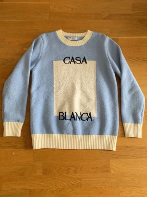 Ljusblå stickad tröja  - Ljusblå stickad tröja med krämvita ribbade muddar och nederkant. Stor rektangel i offwhite på bröstet och svart text. Mjuk och fluffig känsla, perfekt för kyliga dagar.