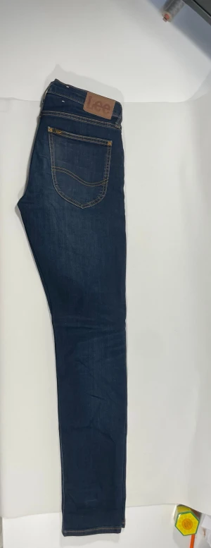 Mörkblå taper jeans från Lee - Snygga mörkblå taper jeans från Lee med klassiska kontrastsömmar och femficksmodell. Jeansen har en smal passform och är tillverkade i stretchigt denimtyg för extra komfort. Perfekta för en avslappnad och trendig look.