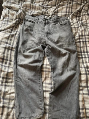 Grå vintage jeans från Wrangler - Säljer ett par grå jeans från Wrangler med klassisk femficksmodell och raka ben. Jeansen har en snygg tvättad look och är tillverkade i slitstarkt denimtyg. Perfekta för en avslappnad och trendig stil.
