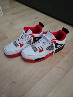 Vita och svarta Air Jordan sneakers - Säljer ett par snygga Air Jordan sneakers i vitt, svart och rött. Skorna har den klassiska Jumpman-loggan på hälen och en låg siluett. Insidan är röd och yttermaterialet är en mix av läder och textil. Perfekta för dig som vill sticka ut med din stil. Priset kan diskuteras