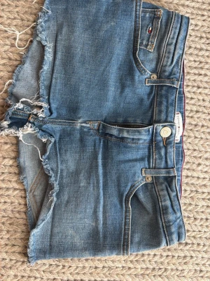 Tommy Hilfiger shorts  - Säljer dessa blåa jeans shorts från Tommy hilfiger. Mid waist. Ganska korta. De är använda men bra skick. Storlek 176 men motsvarar ca 32-34 i storlek eller W24