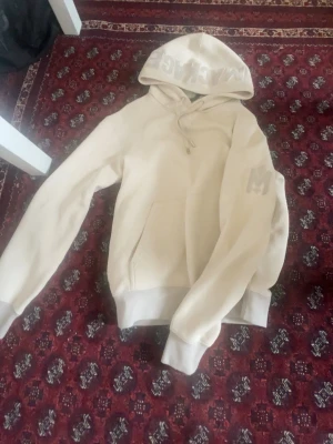 Beige hoodie med tryck från Mackage - Beige hoodie från Mackage med stor huva och tryck på utsidan av huvan. Passar s och m
