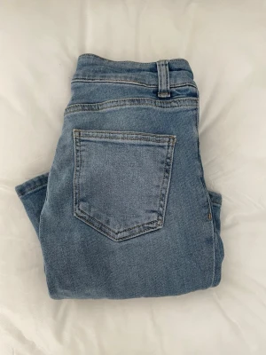 Utåtsvängda ljus blå jeans - Säljer ett par ljusblå jeans med rak passform och klassisk femficksdesign. Jeansen har bälteshällor och knappgylf. Perfekta till en avslappnad stil och passar till det mesta i garderoben.