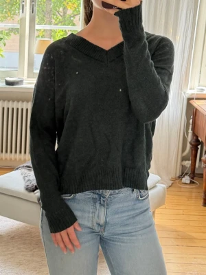 Mörkgrön stickad tröja med v-ringning - Mysig mörkgrön stickad tröja med v-ringad hals och långa ärmar. Tröjan har ribbstickade muddar vid ärmslut och nederkant, samt en avslappnad passform. 