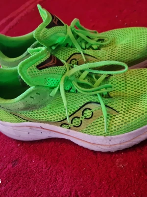 Neongröna Saucony löparsneakers - Säljer ett par neongröna sneakers från Saucony med ventilerande mesh-ovandel och vita sulor. Skorna har klassisk låg design, snörning och Saucony-logga på sidan. Perfekta för dig som vill sticka ut med färg på löprundan.