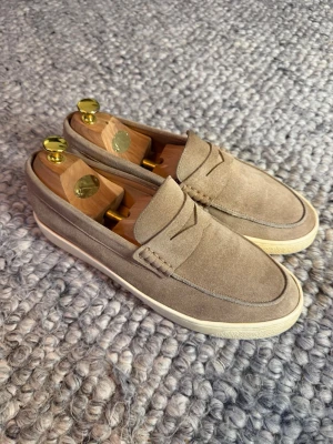 Brunello Cucinelli loafers  - Snygga loafers i beige mocka med klassisk pennyloafers-design och vit gummisula. Skorna har en stilren och tidlös look med rundad tå och diskreta sömmar. Perfekta för dig som gillar en clean och avslappnad stil.
