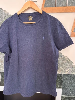 Blå t-shirt från Polo Ralph Lauren - En klassisk mörkblå t-shirt från Polo Ralph Lauren med rund halsringning och den ikoniska broderade loggan på bröstet. Tillverkad i mjuk bomull och har en normal passform. Perfekt basplagg för alla tillfällen.