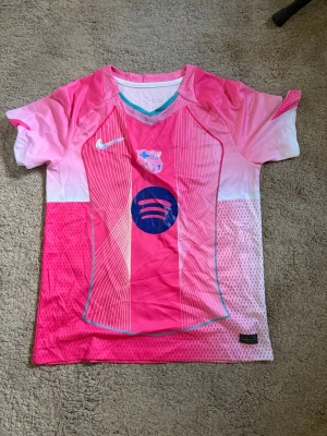 FC Barcelona rosa matchtröja Nike - Snygg FC Barcelona matchtröja i rosa och vitt med blå detaljer. Tröjan har tryck med Lamine Yamal och nummer 19 på ryggen samt klubbmärke och sponsorlogga på bröstet. Tillverkad i lätt och ventilerande material, perfekt för fotboll eller träning.