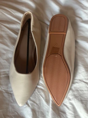 Beige spetsiga ballerinaskor - Snygga ballerinaskor i beige med spetsig tå och låg klack. Skorna har en slät ovansida och en brun sula med vågmönster undertill. Skorna är helt oanvända, bara legat i garderoben tyvärr🤗🥰 storleken är rätt stor, skulle säga 39/40 