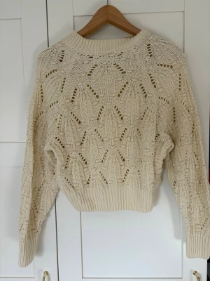 Beige stickad tröja med hålmönster - Säljer en beige stickad tröja med snyggt hålmönster och bred ribbad mudd vid ärmslut och nederkant. ( Trendig).