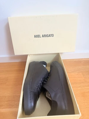  Axel Arigato - Stilrena svarta sneakers från Axel Arigato i slät läder med diskret guldfärgad logga på sidan. Klassisk låg modell med svarta skosnören och gummisula. Perfekta för dig som gillar minimalistisk och clean stil. Storlek 45