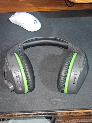 Trådlösa Hyper X hörlurar - Säljer ett par trådlösa over-ear gaminghörlurar i svart och grått med gröna detaljer. Hörlurarna har vadderade kåpor och bygel för extra komfort samt flera knappar och anslutningar på sidorna. Perfekta för gaming eller musik.