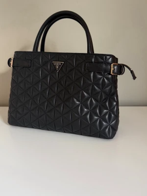 Svart handväska från Guess - Snygg svart handväska från Guess i nyskick. Köpt för 1800kr!☺️                                         Höjd: 22 cm i storlek One Size Längd: 32 cm i storlek One Size Vidd: 11 cm i storlek One Size