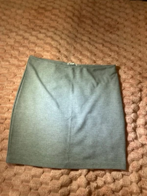 Grå enkel kortkjol - Säljer en stilren grå kortkjol i mjukt material. Kjolen har en rak passform och är perfekt för dig som gillar minimalistisk stil. Enkel att matcha med olika toppar och accessoarer.